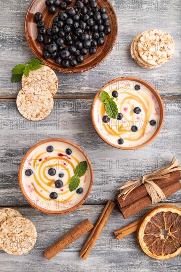 Yoghurt with bilberry and caramel in clay bowl on gray wooden background. top view, flat lay, close up