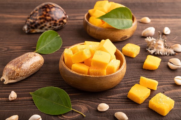 Dried and candied mango cubes in wooden bowls on brown wooden textured background. Side view, close up, vegan, vegetarian food concept