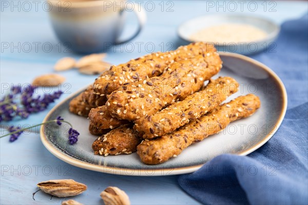 Crumble cookies with seasme and almonds on ceramic plate with cup of coffee and blue linen textile on blue wooden background. side view, close up, selective focus