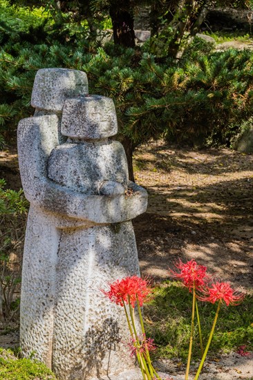 Stone carved statue of two figures behind tiger lily flowers in mountain park in Gimje-si, South Korea, Asia