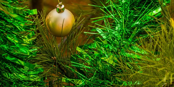 Closeup of gold Christmas ornament and green tensile garland hanging on pine tree in local park in South Korea