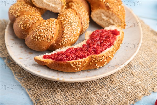 Homemade sweet bun with raspberry jam and cup of coffee on a blue wooden background and linen textile. side view, close up, selective focus