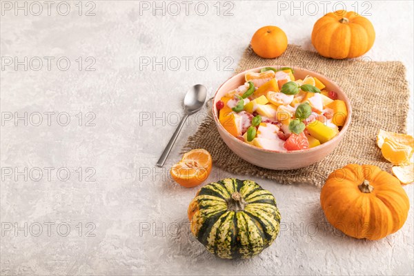 Vegetarian fruit salad of yogurt pumpkin, tangerine, pomegranate, grapefruit, basil microgreen sprouts on gray concrete background and linen textile. Side view, copy space
