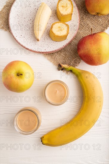 Baby puree with fruits mix, apple, banana infant formula in glass jar on white wooden background. Top view, flat lay, close up, artificial feeding concept