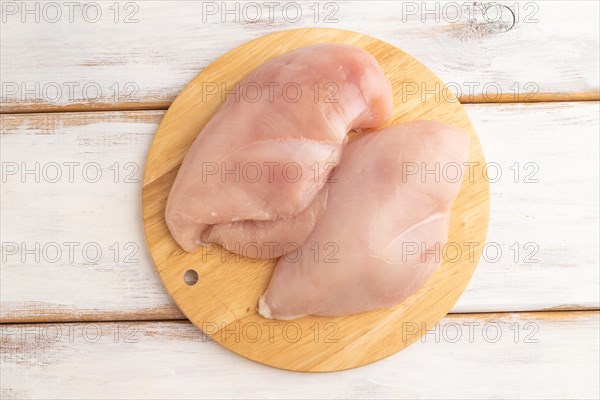 Raw chicken breast with herbs and spices on a wooden cutting board on a white wooden background. Top view, flat lay, close up