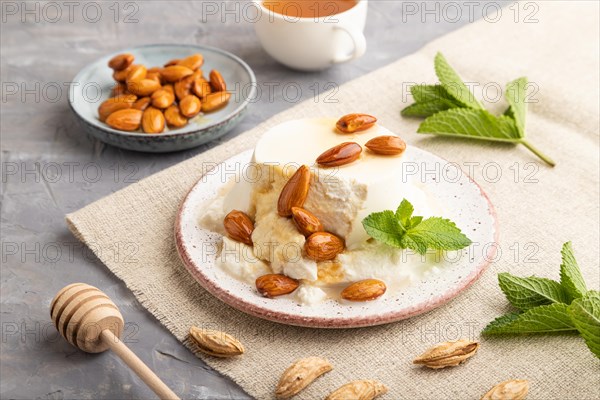 Ricotta cheese with honey and almonds on gray concrete background and linen textile. side view, close up