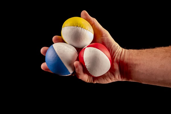 Male hand holding 3 colourful juggling balls, black background, studio shot, Germany, Europe