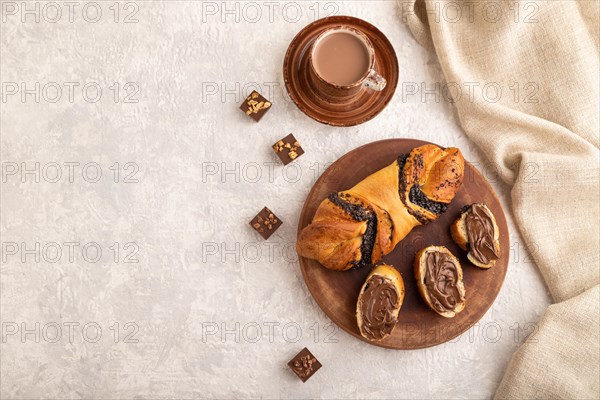 Homemade sweet bun with chocolate cream and cup of coffee on a gray concrete background and linen textile. top view, flat lay, copy space