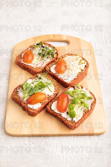 Red beet bread sandwiches with cream cheese, tomatoes and microgreen on gray concrete background. side view, close up