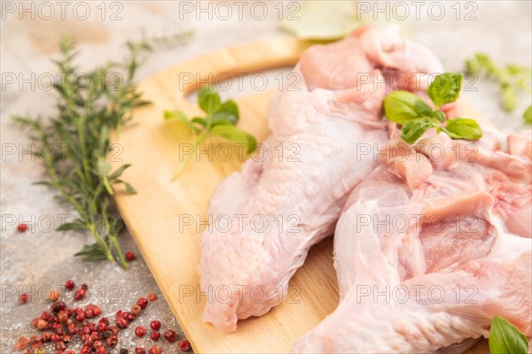 Raw turkey wing with herbs and spices on a wooden cutting board on a brown concrete background. Side view, close up, selective focus