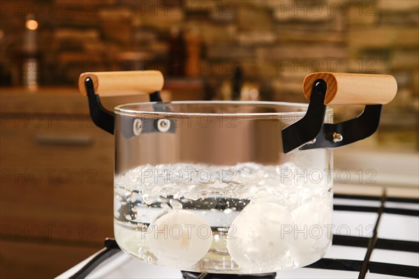 Closeup view of transparent glass saucepan with boiling eggs on a gas stove