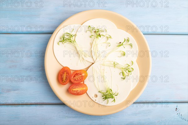 White cheese with tomatoes and cilantro microgreen on blue wooden background. top view, flat lay, close up