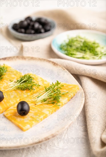 Marble cheese with olives and watercress microgreen on gray concrete background and linen textile. side view, close up, selective focus