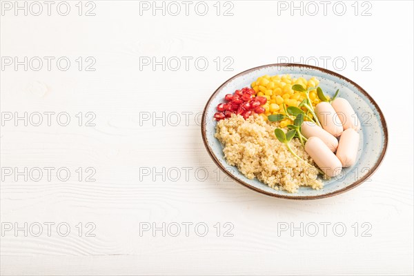 Mixed quinoa porridge, sweet corn, pomegranate seeds and small sausages on white wooden background. Side view, copy space. Food for children, healthy food concept