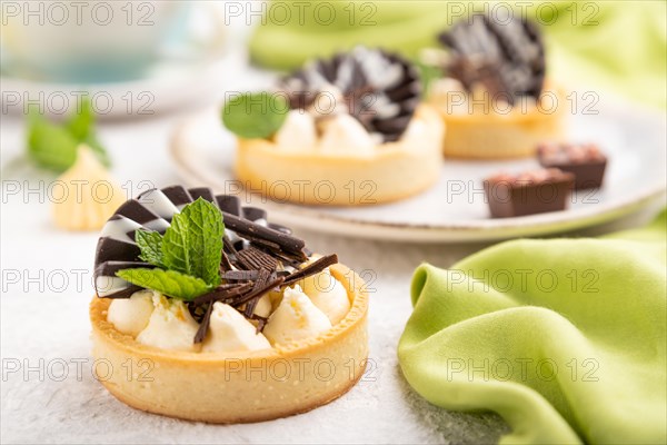 Sweet tartlets with chocolate and cheese cream with cup of coffee on a gray concrete background and green textile. Side view, close up, selective focus