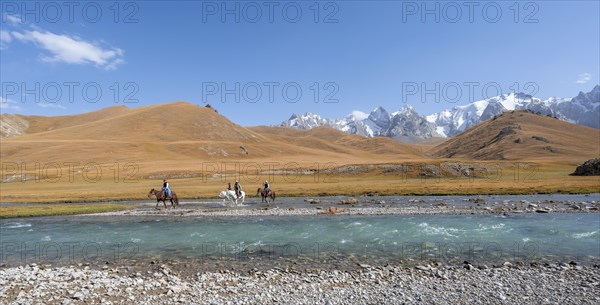 Riders on horses on the river bank, mountain landscape with yellow meadows and river Kol Suu, mountain peak with glacier, hike to the mountain lake Kol Suu, Keltan Mountains, Sary Beles Mountains, Tien Shan, Naryn Province, Kyrgyzstan, Asia