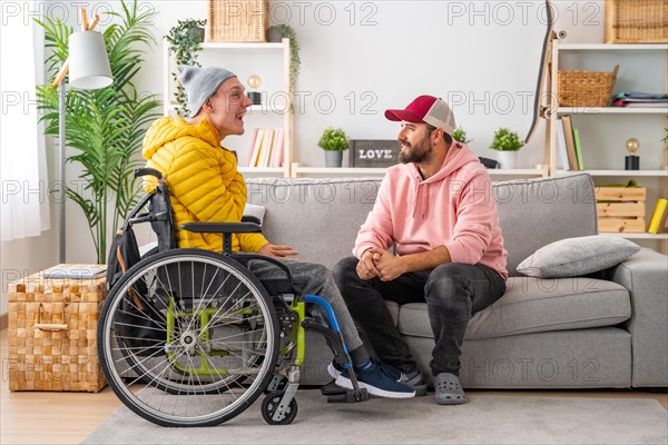 Disabled man in wheelchair and friends chatting relaxed in the living room of the house