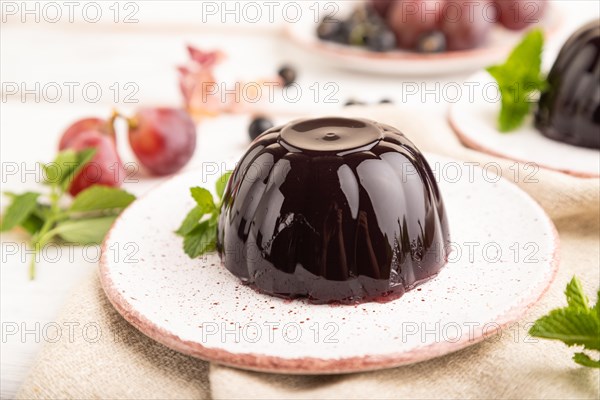 Black currant and grapes jelly on white wooden background and linen textile. side view, close up, selective focus