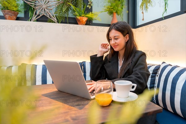 Young businesswoman using laptop in a cafeteria in the morning while drinking juice and coffee