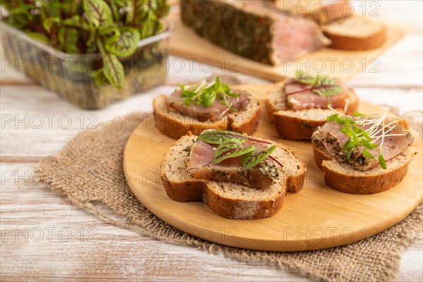 Bread sandwiches with jerky salted meat, sorrel and cilantro microgreen on white wooden background and linen textile. side view, close up, selective focus