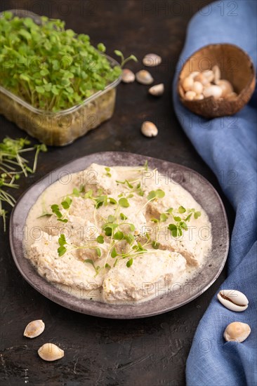 Stewed chicken fillets with coconut milk sauce and rucola microgreen on black concrete background and blue linen textile. side view, close up, selective focus