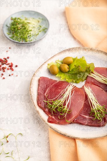 Slices of smoked salted meat with cilantro microgreen on gray concrete background and orange textile. Side view, close up, selective focus