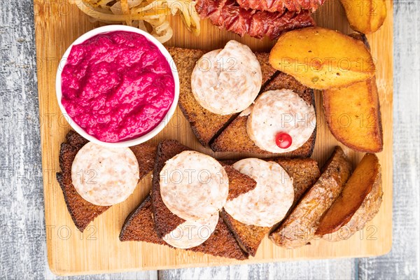 Set of snacks: sausages, toast, sauerkraut, marinated onion and cucumber, baked potato on a cutting board on a gray wooden background. Top view, flat lay, close up