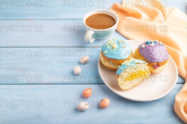 Purple and blue glazed donut and cup of coffee on blue wooden background and orange linen textile. side view, copy space. Breakfast, morning, concept