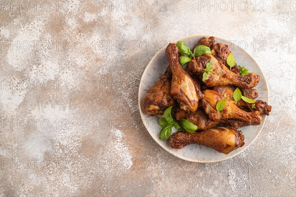 Smoked chicken legs with herbs and spices on a ceramic plate on a brown concrete background. Top view, flat lay, copy space
