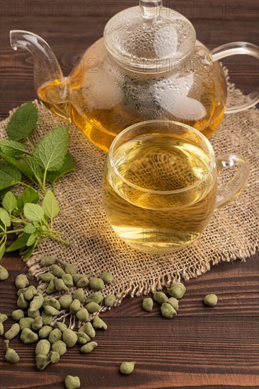 Green oolong tea with herbs in glass on brown wooden background and linen textile. Healthy drink concept. Side view, close up