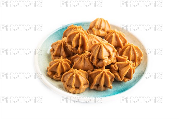 Homemade soft caramel fudge candies on blue plate isolated on white background. side view, close up