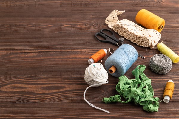 Sewing accessories: scissors, thread, thimbles, braid on brown wooden background. Side view, copy space