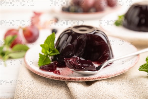 Black currant and grapes jelly on white wooden background and linen textile. side view, close up, selective focus