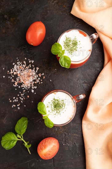 Tomato juice with basil, himalayan salt and sour cream in glass on a black concrete background with orange textile. Healthy drink concept. Top view, flat lay, close up