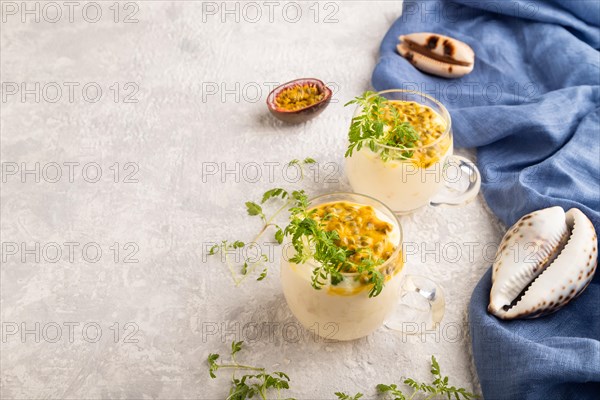 Yogurt with passionfruit and marigold microgreen in glass on gray concrete background with blue linen textile. Side view, copy space