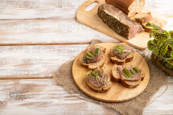 Bread sandwiches with jerky salted meat, sorrel and cilantro microgreen on white wooden background and linen textile. side view, copy space