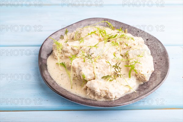 Stewed chicken fillets with coconut milk sauce and mizuna cabbage microgreen on blue wooden background. side view, close up