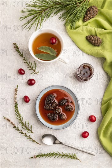 Pine cone jam with herbal tea on gray concrete background and green linen textile. Top view, flat lay, close up
