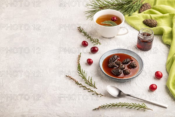 Pine cone jam with herbal tea on gray concrete background and green linen textile. Side view, copy space