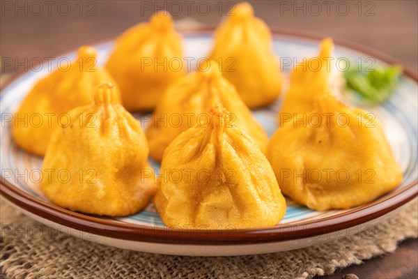 Fried manti dumplings with pepper, basil on brown wooden background and linen textile. Side view, close up, selective focus