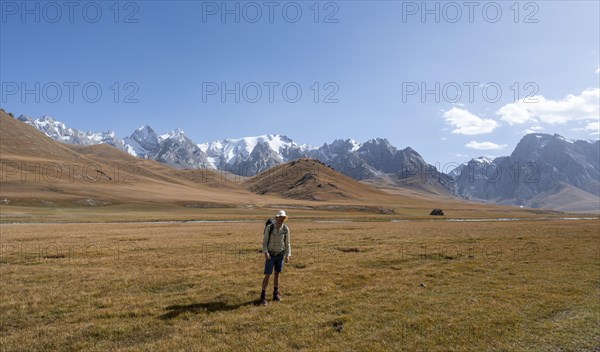 Mountaineer hiking to the mountain lake Kol Suu, mountain landscape with yellow meadows, river Kol Suu and mountain peaks with glacier, Keltan Mountains, Sary Beles Mountains, Tien Shan, Naryn Province, Kyrgyzstan, Asia