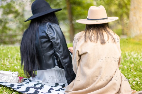 Rear view of two girls looking at the screen of the phone. Back view of two girls in hats looking at the cell phone screen. Concept of two teenage girls looking at the screen of the smart phone