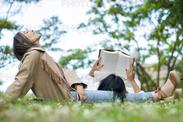 Side view of two relaxed female friends enjoying a day together in the park while getting some fresh air and reading a book