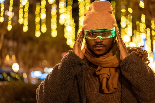 African man in warm clothes using smart glasses at night in the city during Christmas season