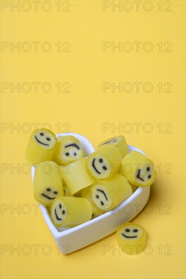 Yellow sweets with smiley in a heart-shaped bowl