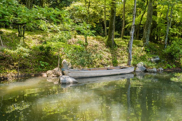 Wooden row boat in water at river bank in Shukkeien gardens in Hiroshima, Japan, Asia