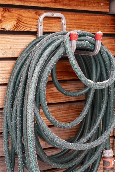 Garden hose covered in hoarfrost hangs on wooden facade