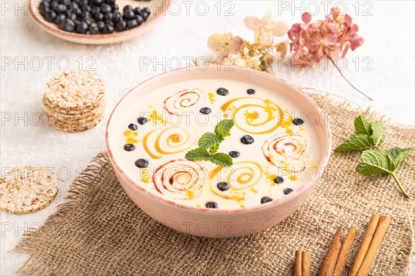Yoghurt with bilberry and caramel in ceramic bowl on gray concrete background and linen textile. side view, close up