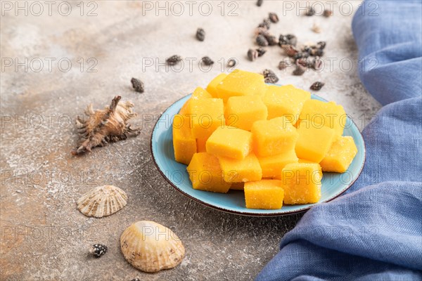 Dried and candied mango cubes on blue plate on brown concrete background and linen textile. Side view, close up, vegan, vegetarian food concept