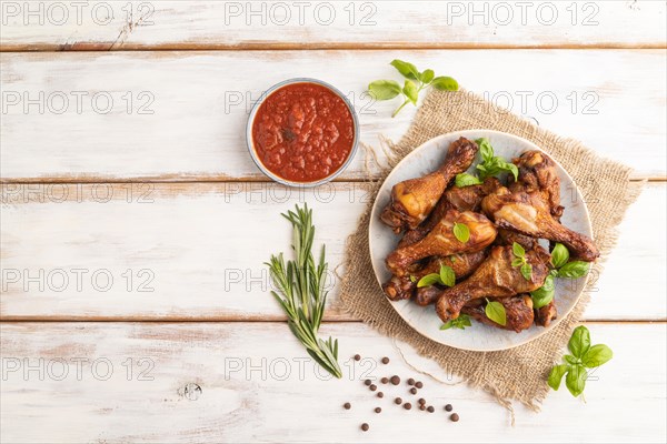 Smoked chicken legs with herbs and spices on a ceramic plate with linen textile on a white wooden background. Top view, flat lay, copy space